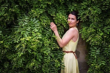 Woman staying surrounded by lush green plants, touching leaves.の写真素材
