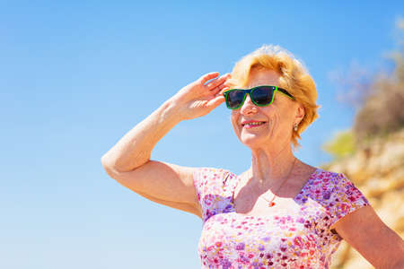 Elderly woman in sunglasses looking at the sea and having fan.の写真素材