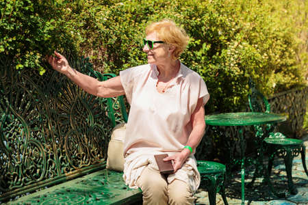 Mature beautiful woman traveler, sits on the bench of the parkの写真素材