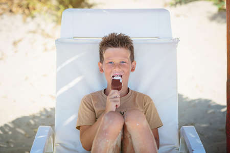Handsome boy sitting on the beach and eating ice creamの写真素材