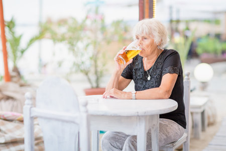 Mature woman sitting at a table in a summer cafe and drinking beerの写真素材
