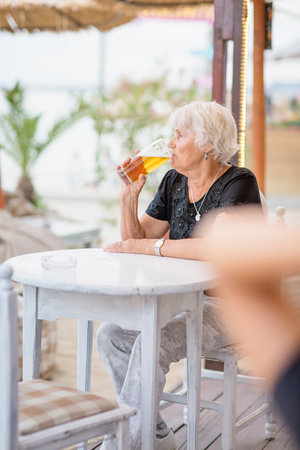 Mature woman sitting at a table in a summer cafe and drinking beerの写真素材
