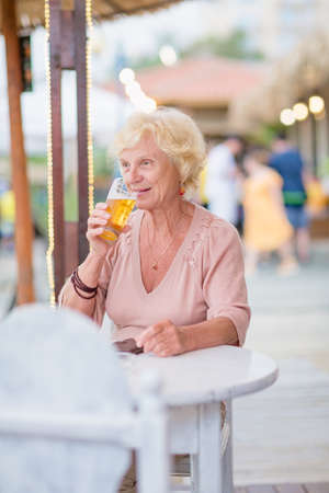 Mature woman sitting at a table in a summer cafe and drinking beerの写真素材