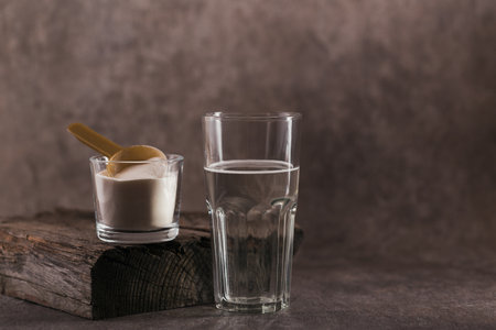 Glass with collagen dissolved in water and collagen protein powder on brown background