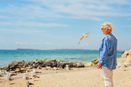 Elderly woman standing on the beach and looking into the distanceの写真素材