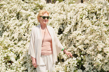 Elderly woman posing among bushes with white flowers