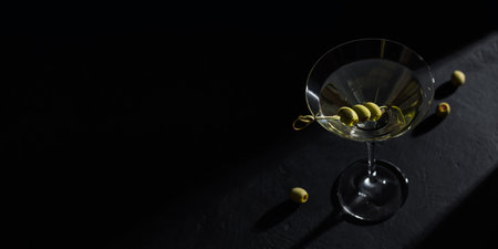 Glass of classic dry martini cocktail with olives on dark stone table against a black background.の写真素材