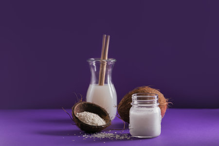 Bottle of coconut vegan milk, coco oil, whole coconut and flakes on violet backgroundの写真素材