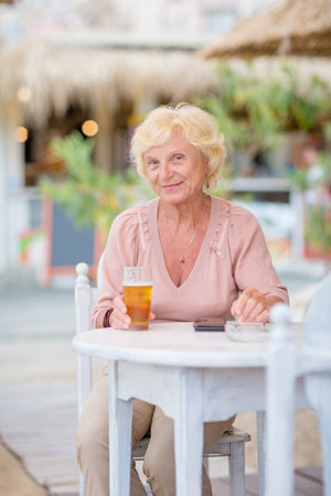 Mature woman sitting at a table in a summer cafe and drinking beerの写真素材