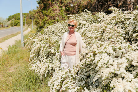 Elderly woman posing among bushes with white flowersの写真素材