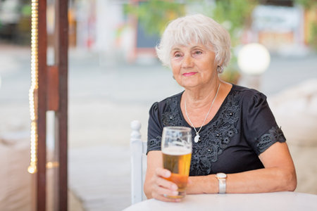 Mature woman sitting at a table in a summer cafe and drinking beerの写真素材