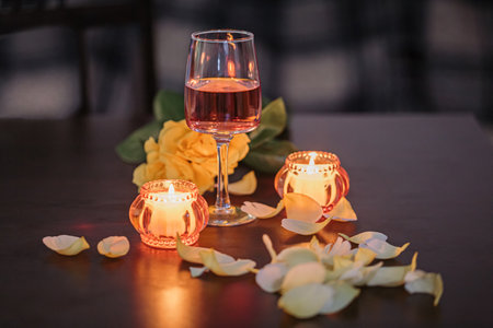 A glass of rose wine, two candles and rose petals on a dark tableの写真素材
