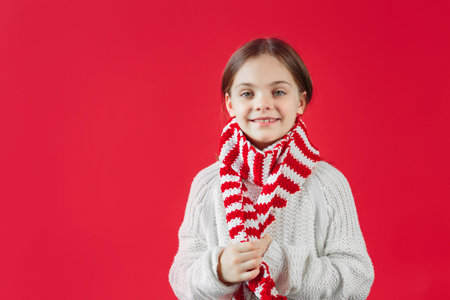 Closeup of a smiling face of young girl in a white sweater and striped scarfの写真素材