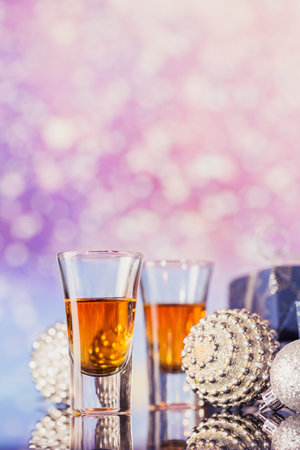 Two glasses of whiskey or bourbon with Christmas decoration on a light bokeh background. New Year,...
