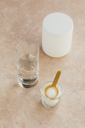 Collagen powder in bowl, glass of water and measure spoon on a light beige background. Extra protein intake. Natural beauty and health supplement concept.の写真素材
