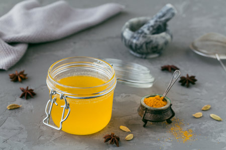 Healthy homemade Ghee or clarified butter in a jar and turmeric powder on grey concrete background....
