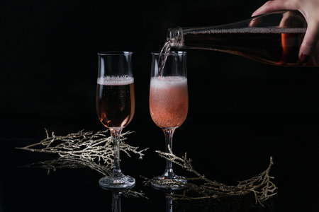 Two glasses of rose champagne and Christmas or New Year decoration on black background. Womans hand...