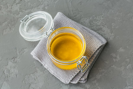 Homemade Ghee or clarified butter in a jar on grey concrete background.
