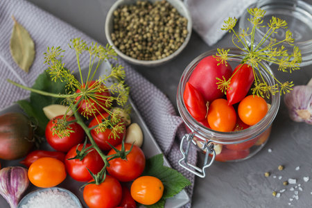 Preserving fresh and pickled tomatoes, seasonings and garlic on grey concrete table. Healthy fermented food. Home canned vegetables.の写真素材