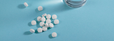 Vitamin white pills freely laid near glass of water on light blue background