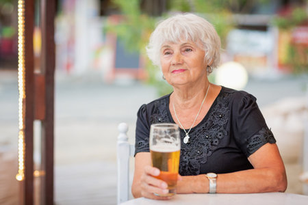 Mature woman sitting at a table in a summer cafe and drinking beerの写真素材