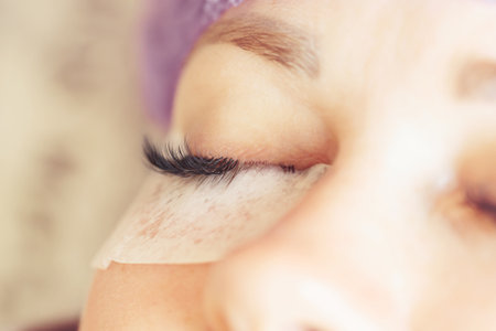 eyelash extension procedure. Female eye with long eyelashes. Professional lash maker working with customer. Lashes close up, macro, selective focus.の写真素材