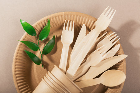 Eco-friendly disposable utensils made of bamboo wood and paper on a light beige background. Fork, knives, plates, paper cups and strawsの写真素材
