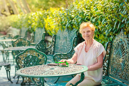 Mature attractive woman traveler sitting alone on the terrace of coffee shop in beautiful park in Bulgaria. Active life of the elderly in retirement, active seniorsの写真素材
