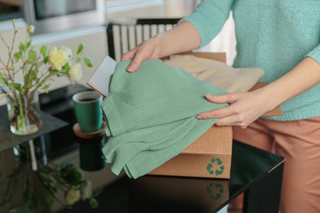 Woman packing box with used wardrobe for reuse. Reusing, recycling materials and reducing waste in...