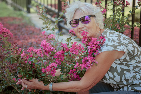 Happy senior woman smelling and touching perple flowers at summer gardenの写真素材