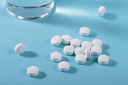 Vitamin white pills freely laid near glass of water on light blue backgroundの写真素材