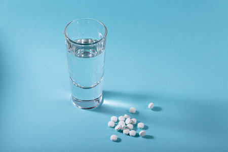 Vitamin white pills freely laid near glass of water on light blue backgroundの写真素材