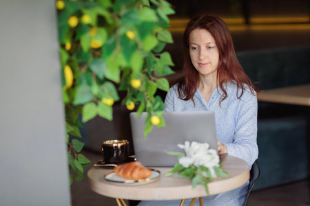 Woman sitting at table, using laptop computer while having coffee in cafeの写真素材