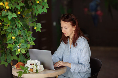 Woman sitting at table, using laptop computer while having coffee in cafeの写真素材