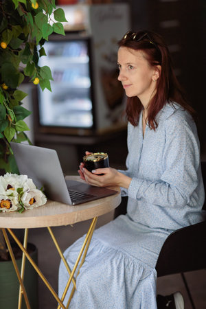 Woman sitting at table, using laptop computer while having coffee in cafeの写真素材