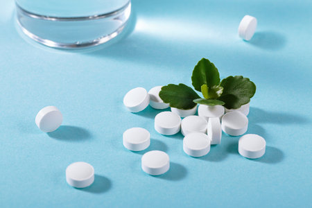 Vitamin white pills freely laid near glass of water on light blue backgroundの写真素材