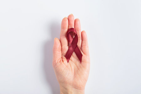 Burgundy cancer ribbon in womans hand on white background