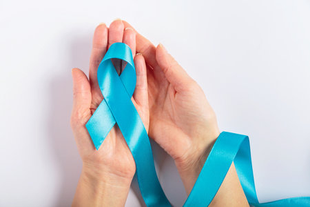 Blue ribbon in hand for cancer awareness on white backgroundの写真素材