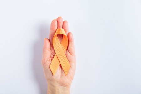 Orange cancer ribbon in womans hand on white backgroundの写真素材
