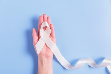 White cancer ribbon in womans hand on blue backgroundの写真素材