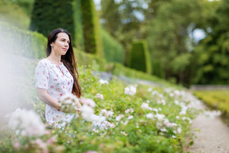 Portrait of attractive woman sitting among white roses in old parkの写真素材