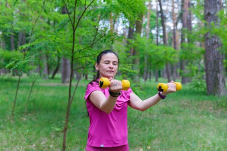 Mature Woman Extending Arms with Dumbbells Outdoorsの写真素材