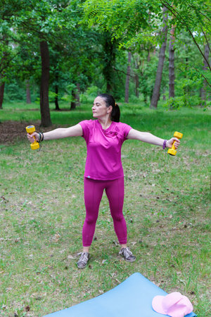 Mature Woman Exercising with Dumbbells in Natureの写真素材