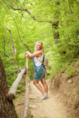 Middle aged woman with backpack walking along forest pathの写真素材
