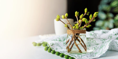 Green spring buds in glass jar and coffee cup on cozy table