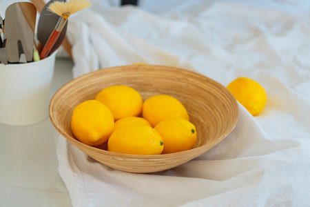 Fresh lemons in a wooden bowl on a white fabric backgroundの写真素材