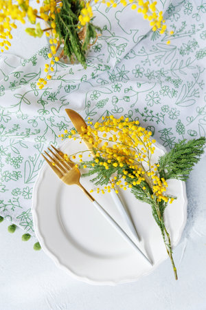 Festive spring table arrangement with mimosa and gold utensilsの写真素材