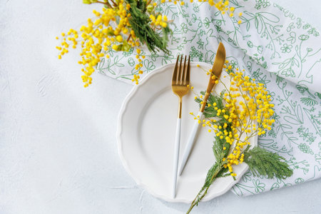 Spring festive table setting with mimosa flowers and golden flatwareの写真素材