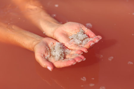 Hands Holding Salt Crystals in Pink Lake