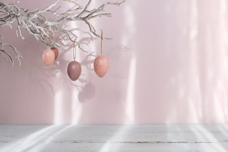 Easter eggs hanging on branch on pastel pink backgroundの写真素材